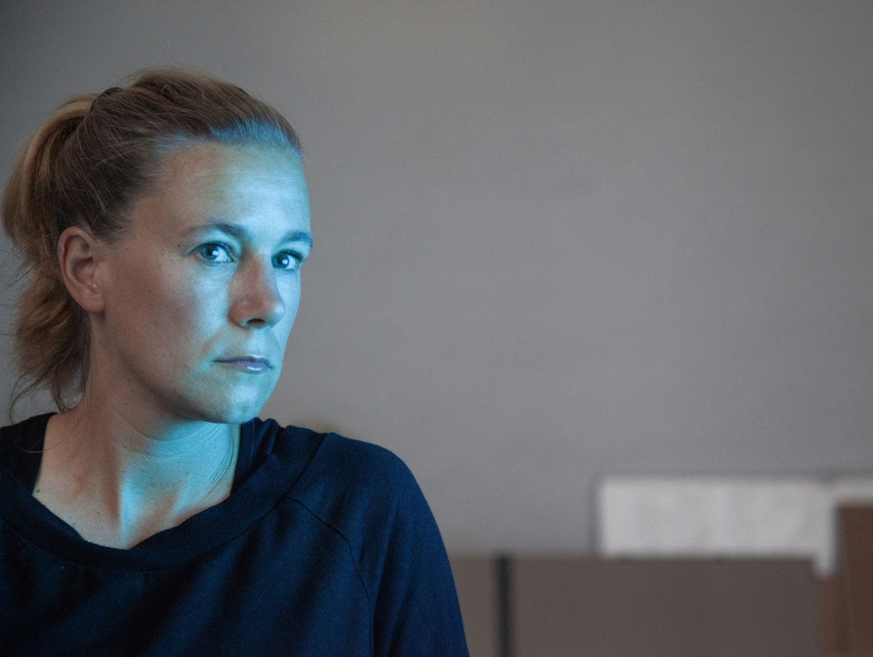 Porträtfoto von Janne Höltermann. Die Künstlerin ist im Halbprofil zu sehen uns ihr Gesicht wird von einem blauen Licht erleuchtet.