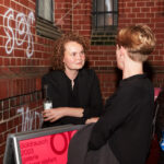 Zwei Personen im Gespräch vor einem roten Backsteingebäude