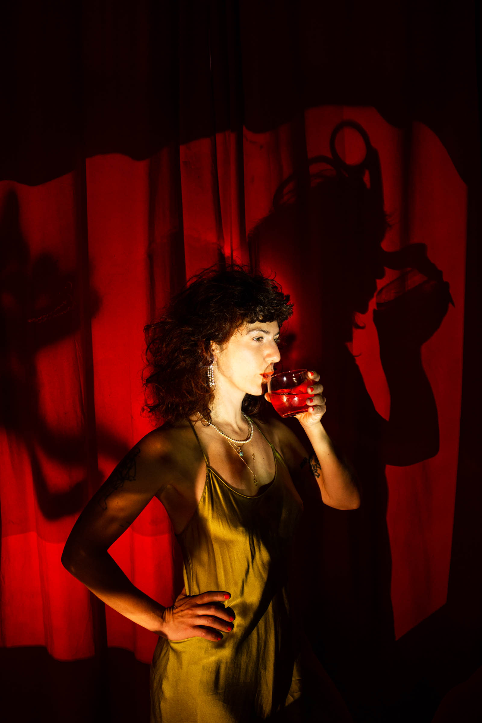 Porträtfoto von Shira Orion. Die Künstlerin steht vor einem roten Vorhang.
