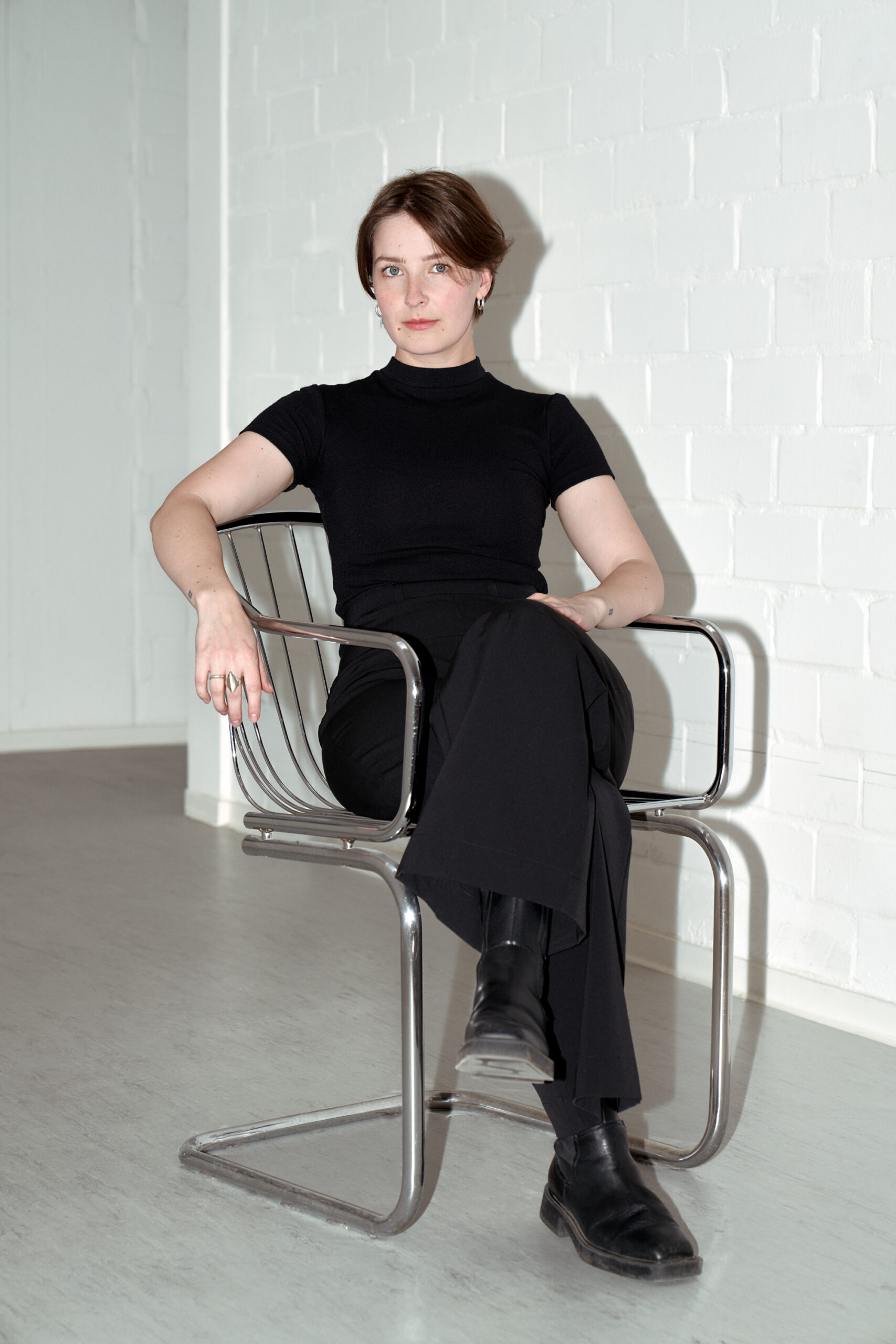 Porträtfoto von Tiziana Krüger. Die Künstlerin sitzt in einem Stuhl und blickt in die Kamera.